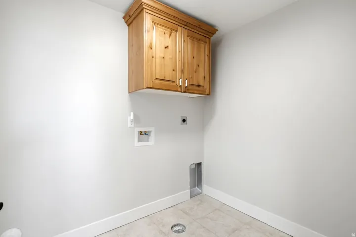 Dedicated laundry space featuring a wood-finish wall cabinet with crown molding, tile flooring, and integrated utility connections