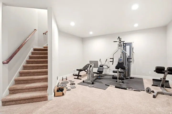 Carpeted staircase with wooden handrail opening to a spacious room featuring recessed lighting and neutral wall tones