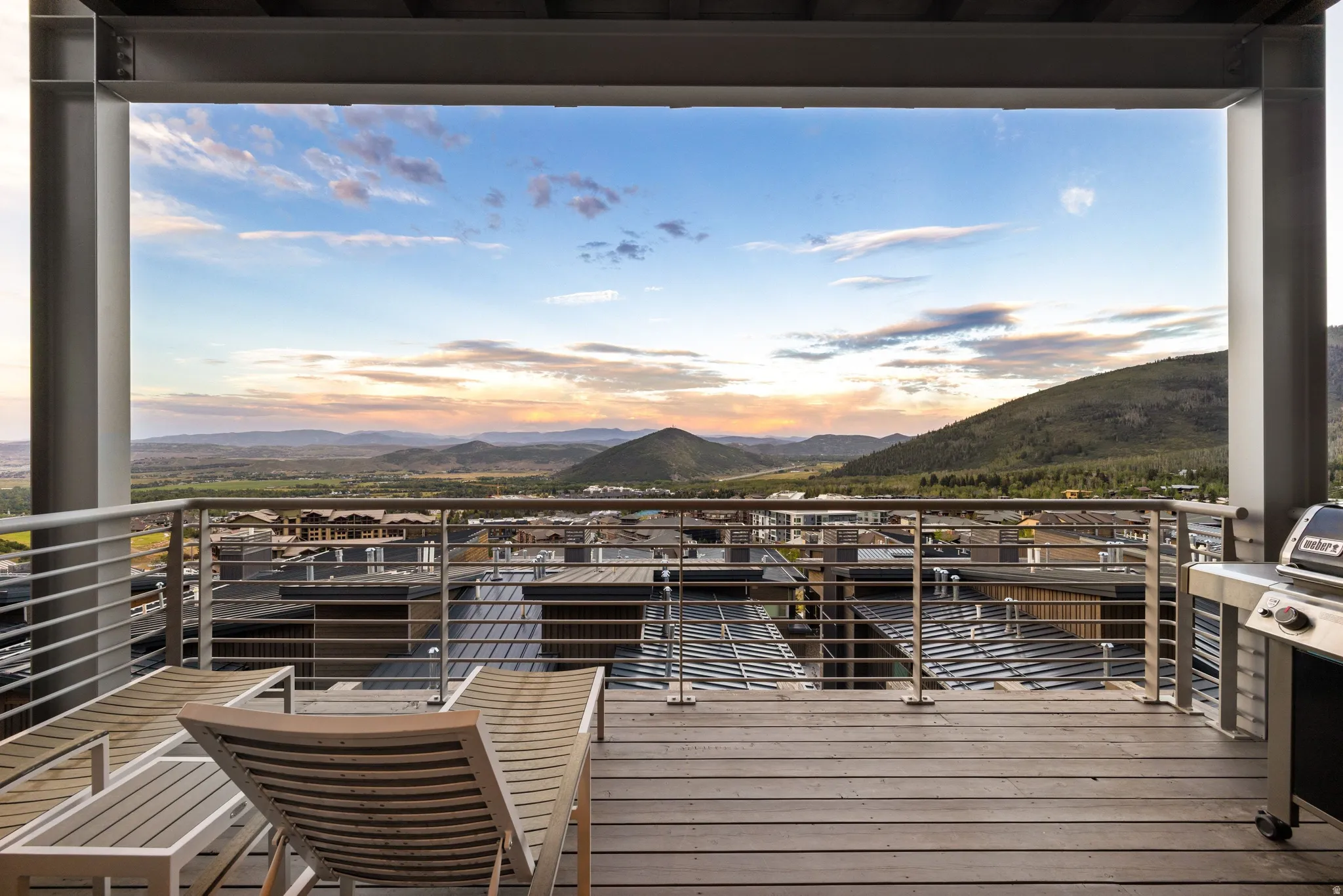 Expansive outdoor deck featuring wood-finish flooring, a metal railing system, structural beams, and distant mountain scenery