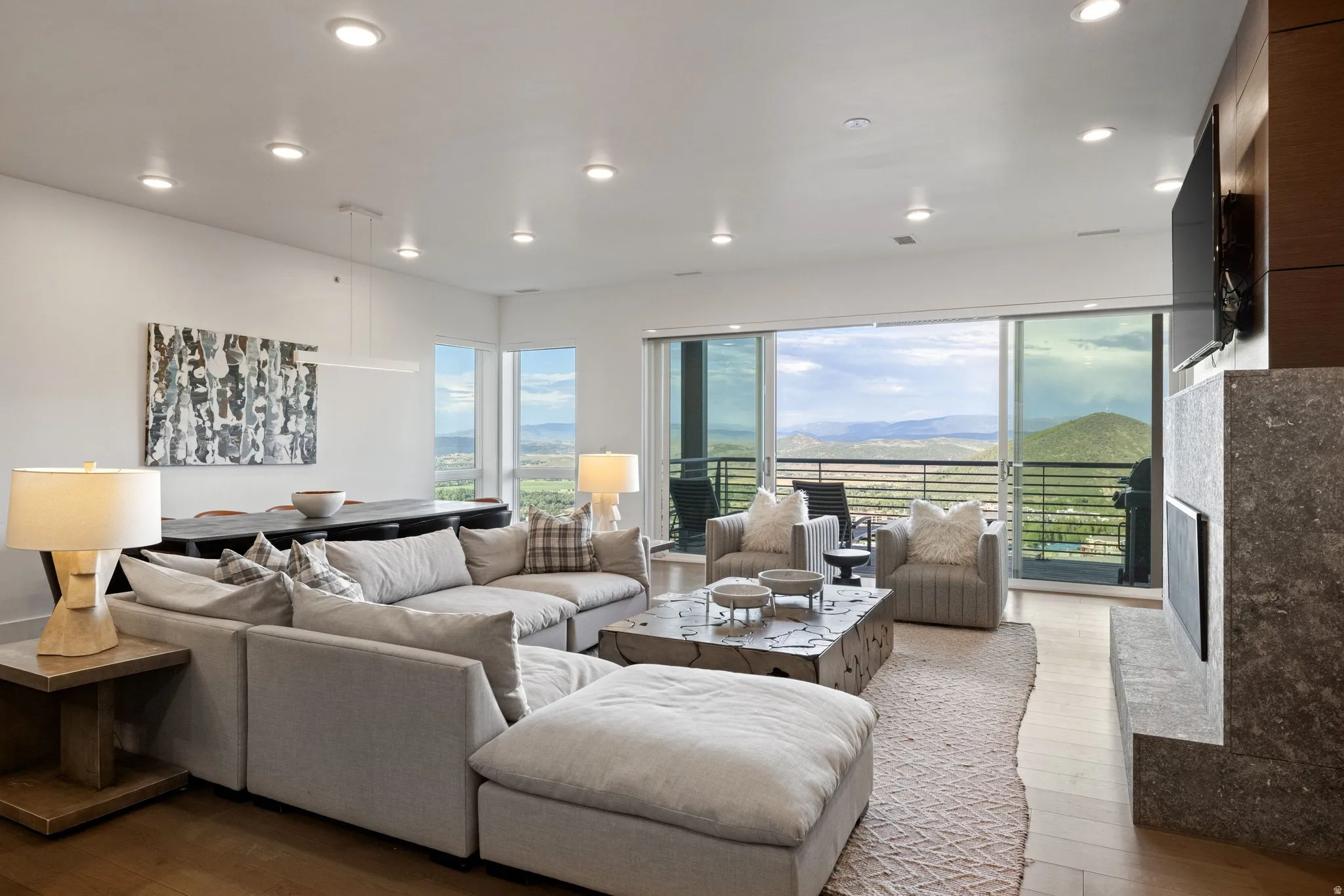 Spacious living area featuring expansive sliding glass doors, recessed lighting, wood-finish flooring, and a contemporary fireplace with a stone surround