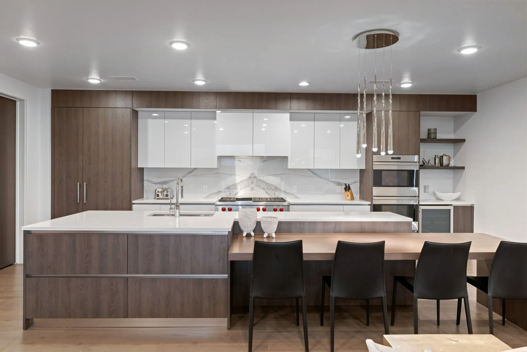 Contemporary kitchen featuring wood-finish cabinetry, white high-gloss upper cabinets, a stone countertop island, and a distinctive linear chandelier