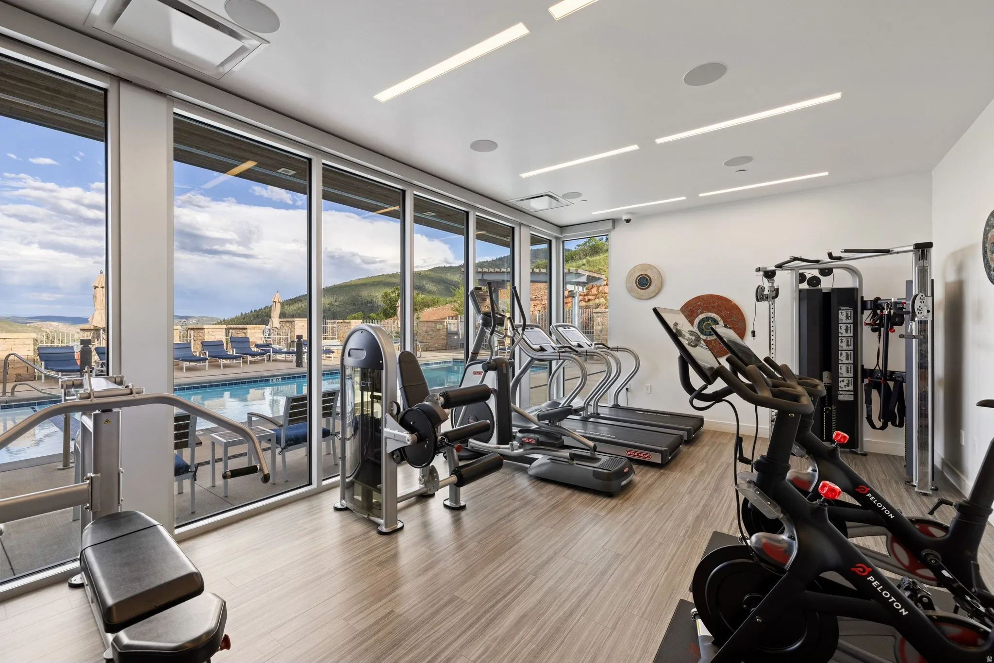 Fitness center featuring expansive floor-to-ceiling windows, recessed lighting, wood-finish flooring, and direct access to an outdoor swimming pool area with lounge seating