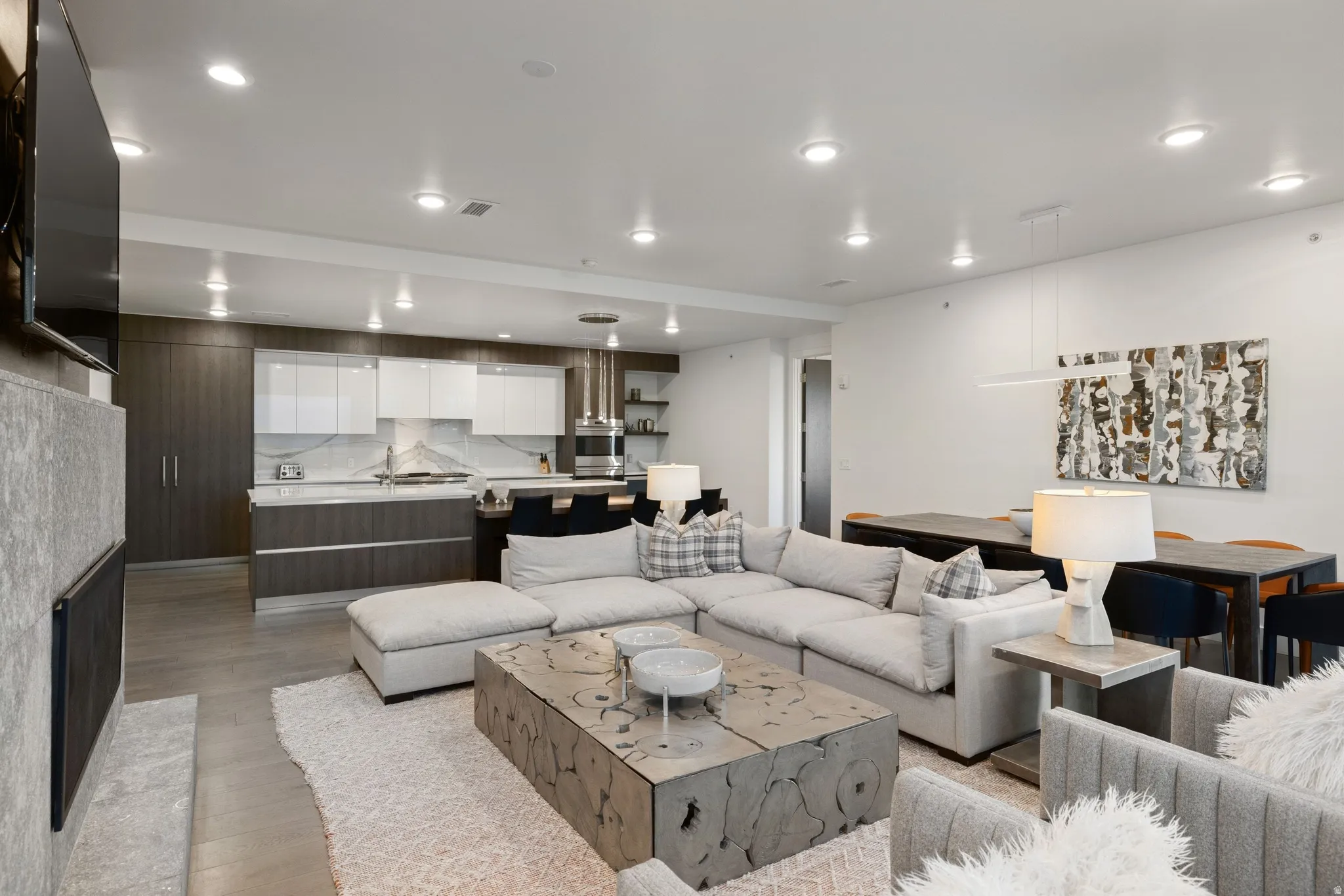Open-concept living space featuring wood-finish flooring, recessed lighting, and a linear electric fireplace with a stone surround