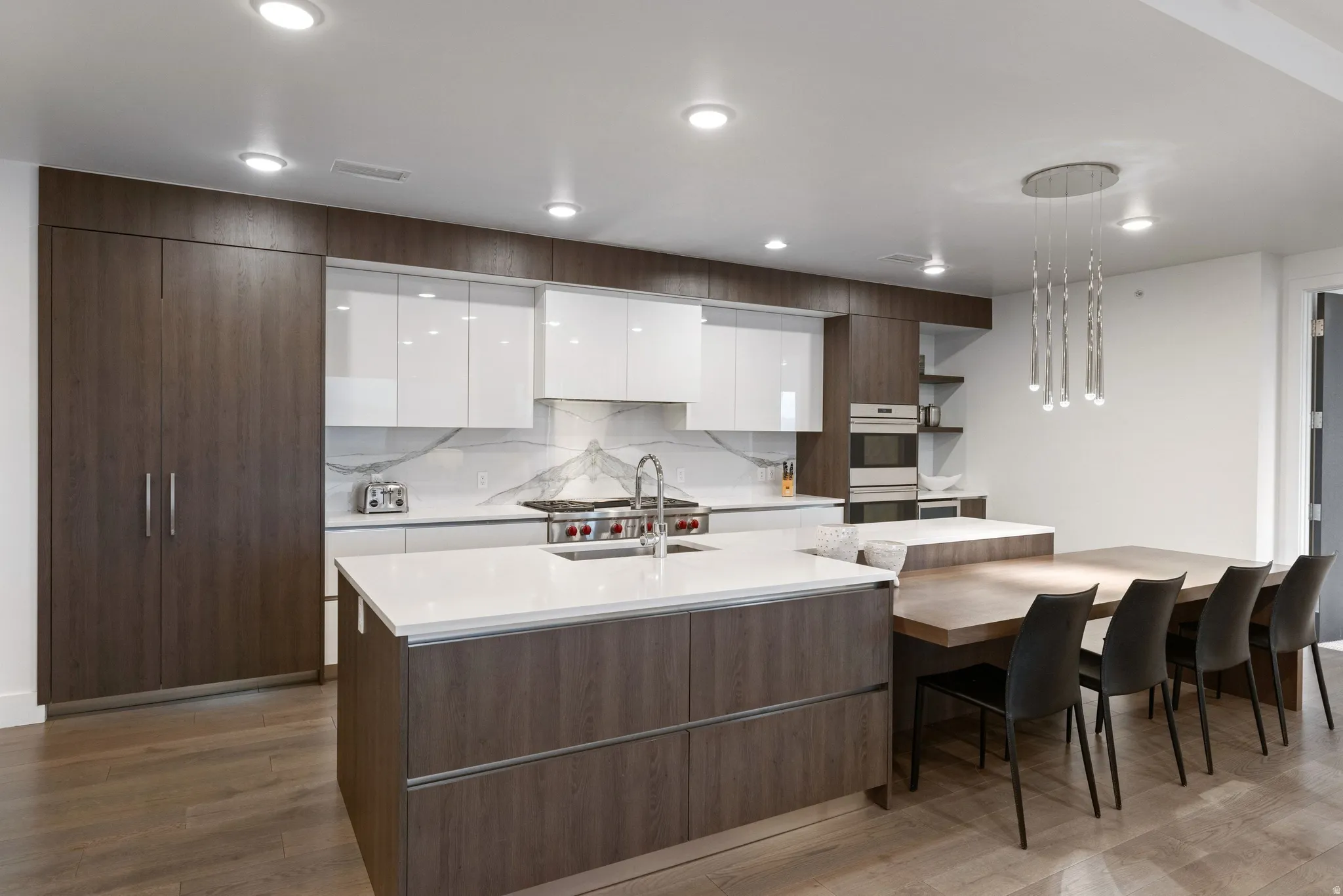 Modern kitchen featuring a large central island with a sink, white countertops, integrated wood-finish cabinetry, and a built-in wall oven