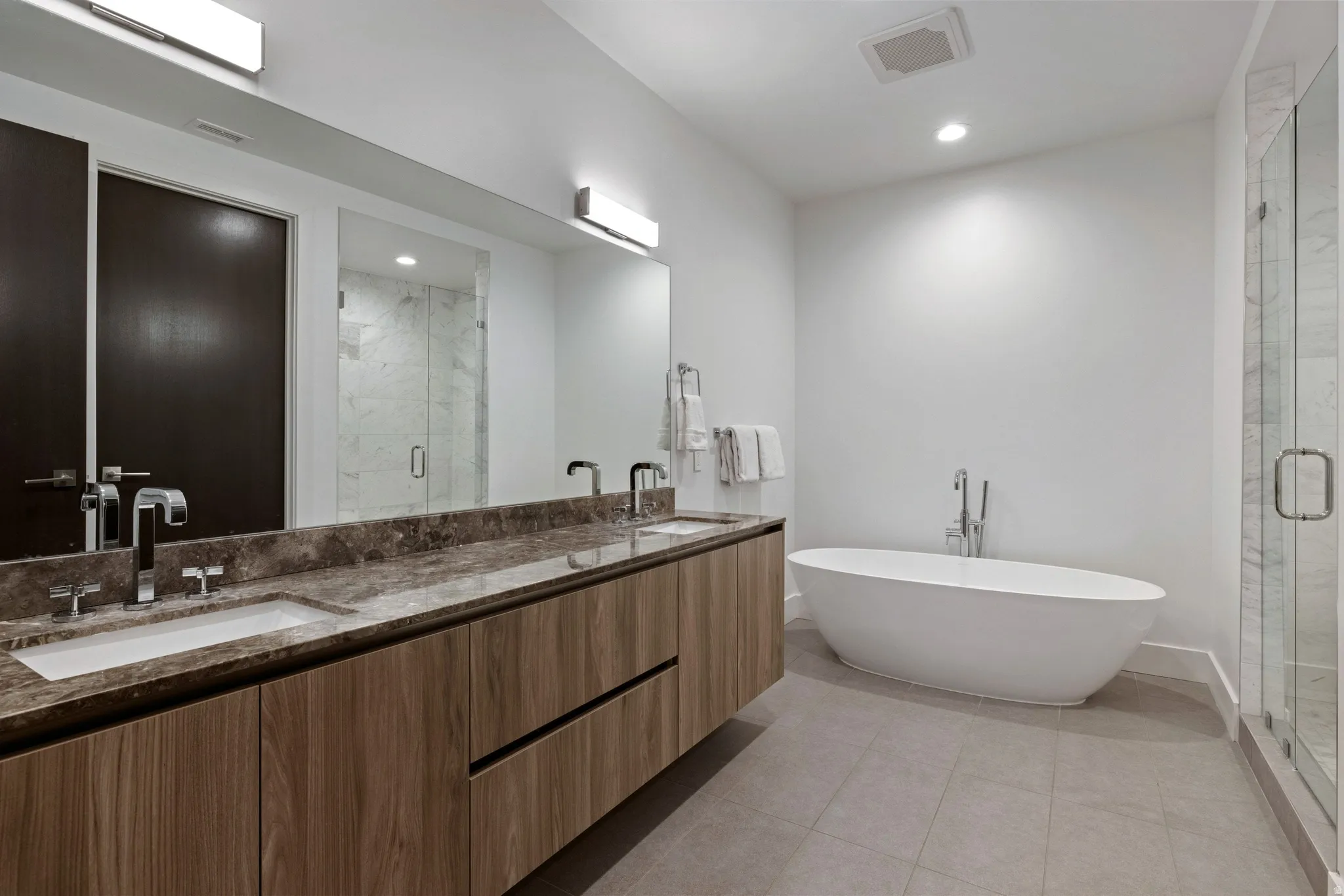 Modern bathroom featuring a freestanding soaking tub, a frameless glass shower enclosure, a dual vanity with a stone countertop, wood-finish cabinetry, and recessed lighting