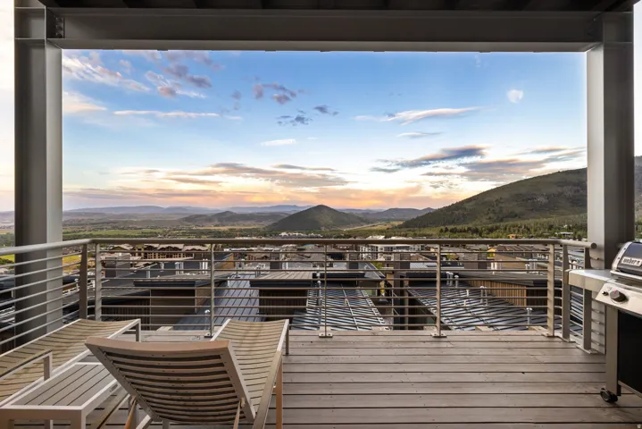 Expansive outdoor deck featuring wood-finish flooring, a metal railing system, structural beams, and distant mountain scenery