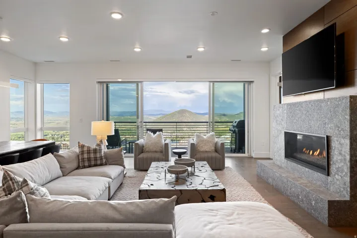 Spacious living area featuring a sleek fireplace with a stone surround, wood-finish flooring, recessed lighting, and expansive sliding glass doors opening to a balcony