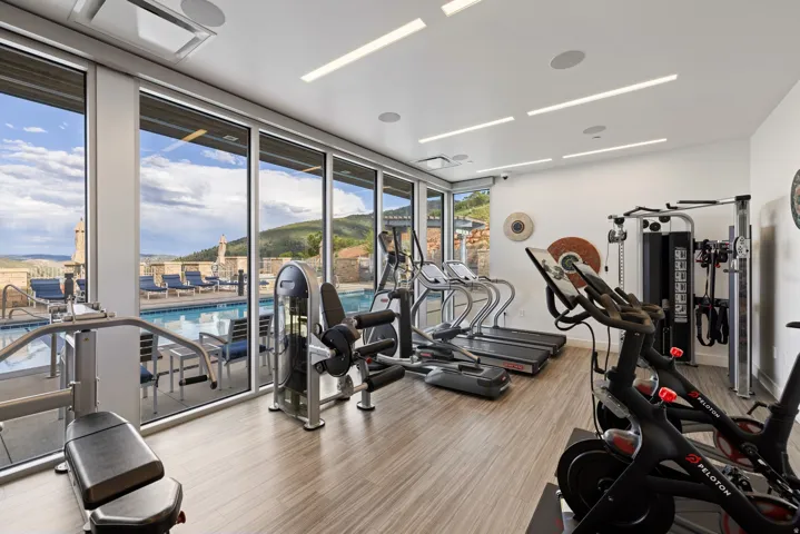Fitness center featuring expansive floor-to-ceiling windows, recessed lighting, wood-finish flooring, and direct access to an outdoor swimming pool area with lounge seating