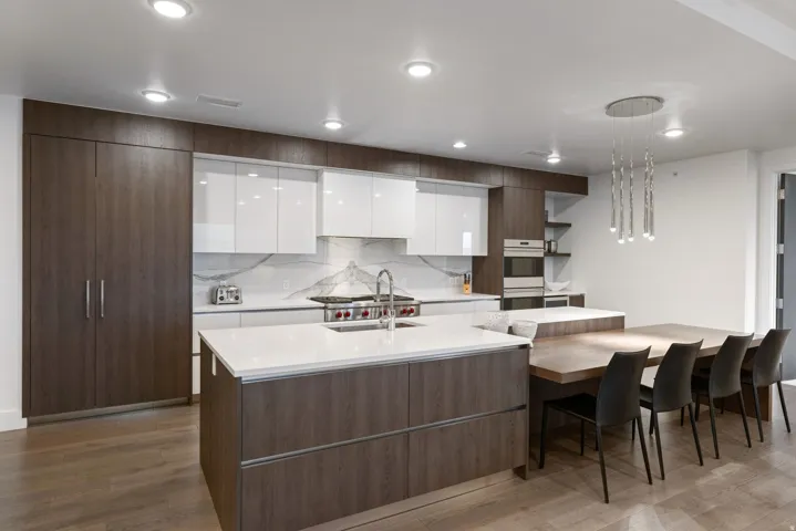 Modern kitchen featuring a large central island with a sink, white countertops, integrated wood-finish cabinetry, and a built-in wall oven