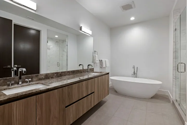 Modern bathroom featuring a freestanding soaking tub, a frameless glass shower enclosure, a dual vanity with a stone countertop, wood-finish cabinetry, and recessed lighting