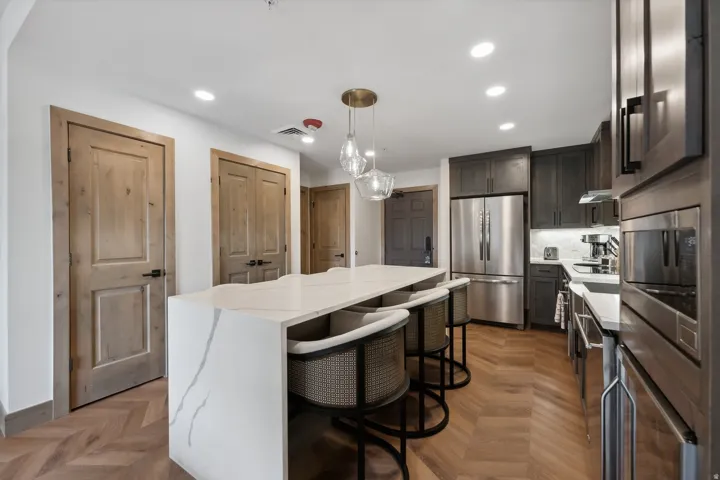 Kitchen featuring a waterfall-edge island with seating, herringbone wood-finish flooring, dark wood cabinetry, stainless steel appliances, and recessed lighting