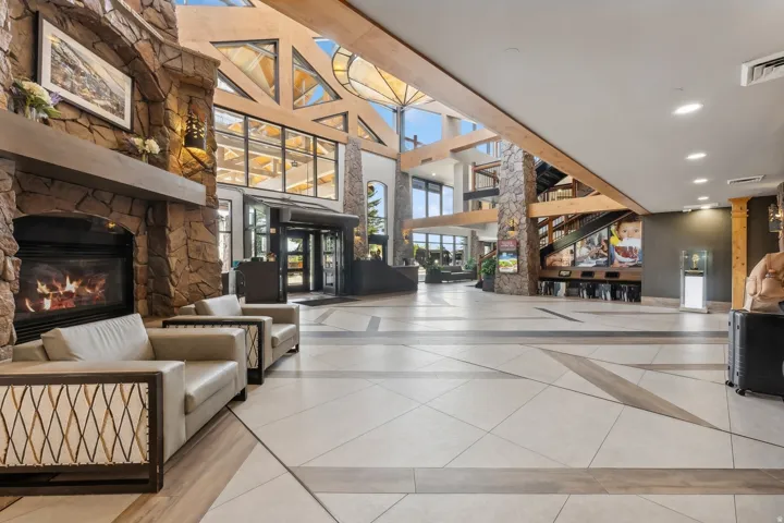 Spacious lobby featuring a stone-clad fireplace, soaring wood-beamed ceilings, geometric window designs, and large format tile flooring