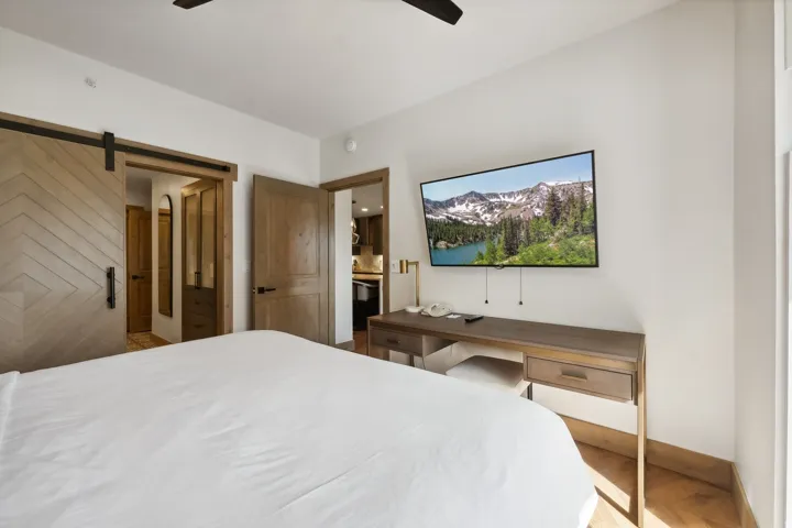 Bedroom featuring a chevron-patterned barn door, wood-finish flooring, a wall-mounted television, and a built-in desk with integrated storage