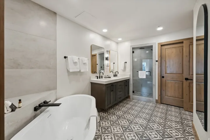 Spacious bathroom featuring a freestanding tub with a matte black faucet, a large walk-in shower with a glass enclosure, a double vanity with ample storage, and patterned floor tiling