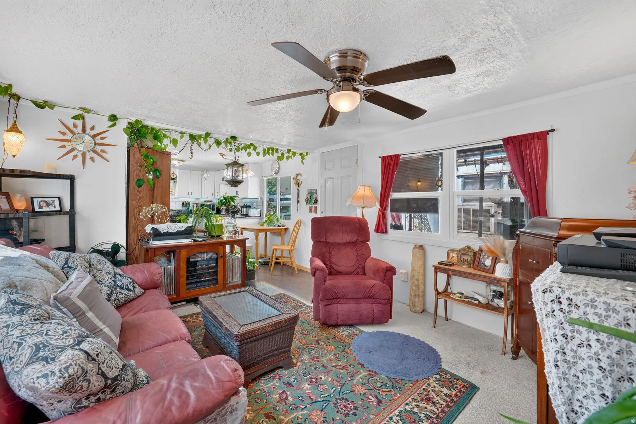 Living area featuring ceiling fan light fixture, white walls, and a window with red drapery