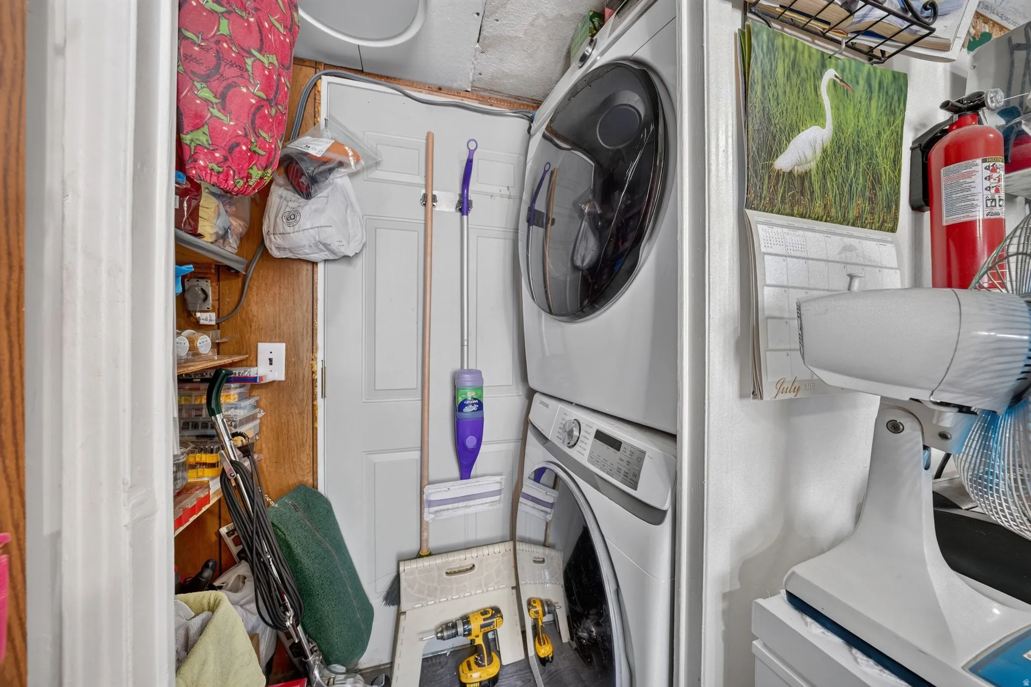 Stackable washer and dryer unit with a white panel door and wall-mounted shelving