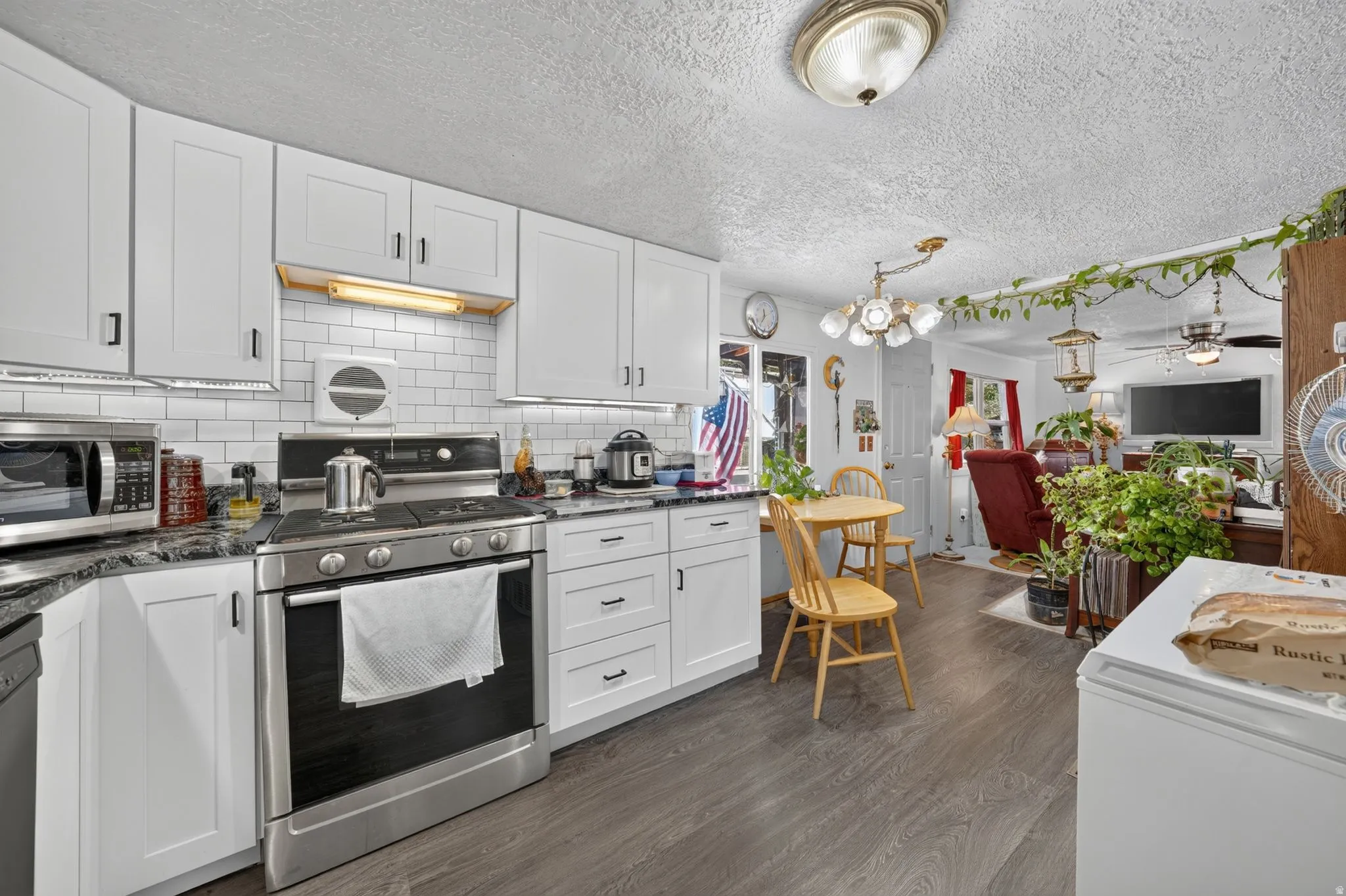 Updated kitchen featuring white shaker-style cabinetry, dark stone countertops, stainless steel appliances, and a white subway tile backsplash