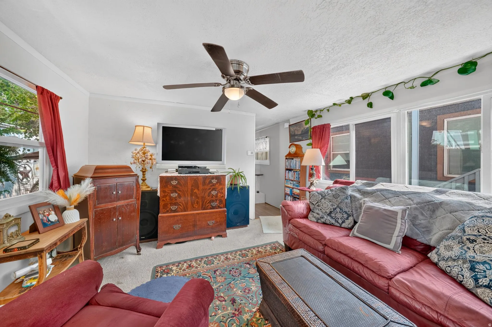 Living area featuring a ceiling fan, wall-mounted display, and expansive windows