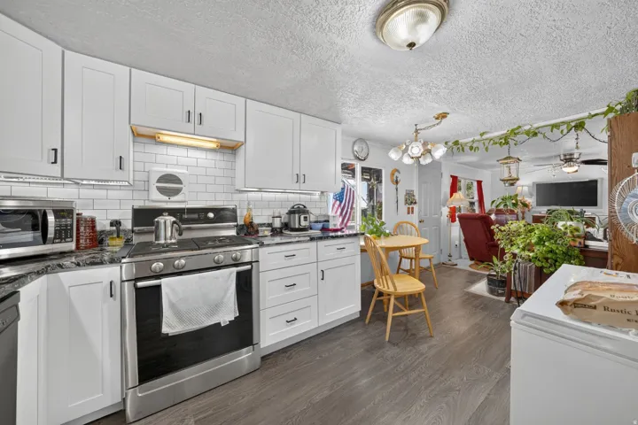Updated kitchen featuring white shaker-style cabinetry, dark stone countertops, stainless steel appliances, and a white subway tile backsplash