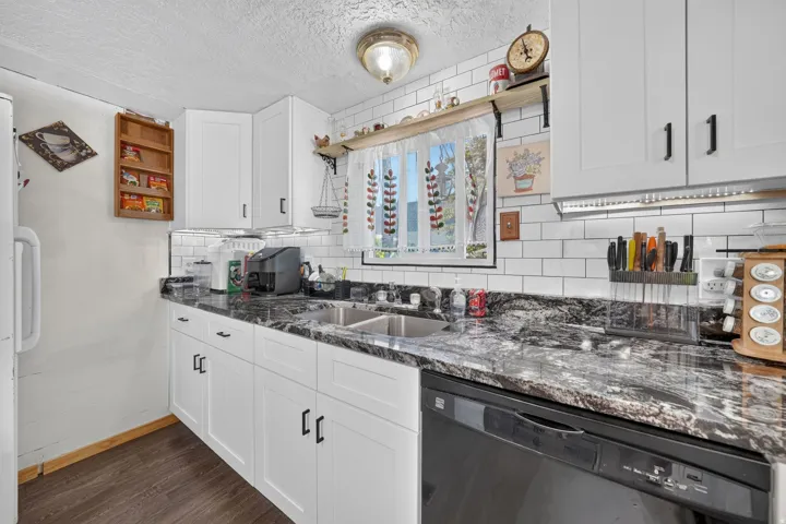 Kitchen featuring white shaker-style cabinetry with matte black hardware, dual-basin stainless steel sink, black and white patterned countertops, subway tile backsplash, and dark wood-finish flooring