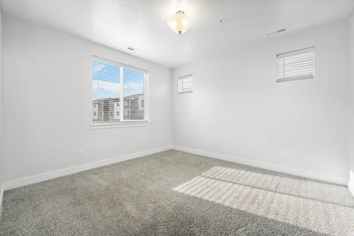 Carpeted primary room featuring a large window with white blinds, two smaller windows with white blinds, a ceiling-mounted light fixture, and white baseboards