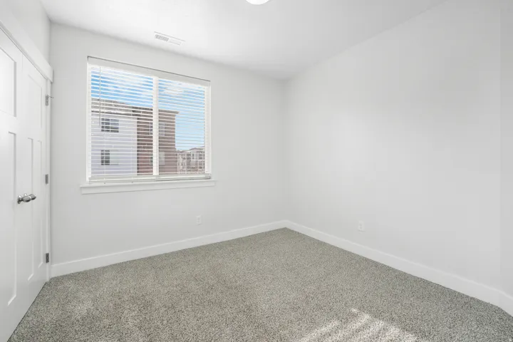 Bright room featuring a large window with horizontal blinds, neutral carpet flooring, white walls, and a contemporary four-panel interior door with chrome hardware