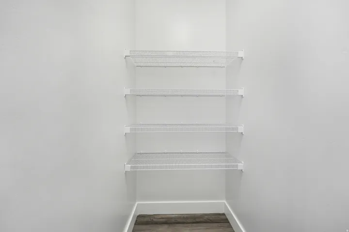 White wire shelving system installed in a closet with light wood-finish flooring and white baseboards