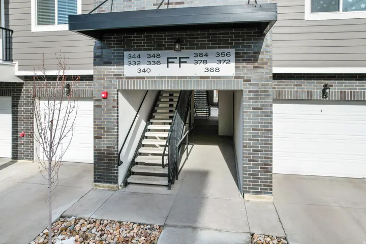 Multi-level building entrance featuring brick masonry, horizontal siding, attached garages, and a prominent exterior staircase with metal railings