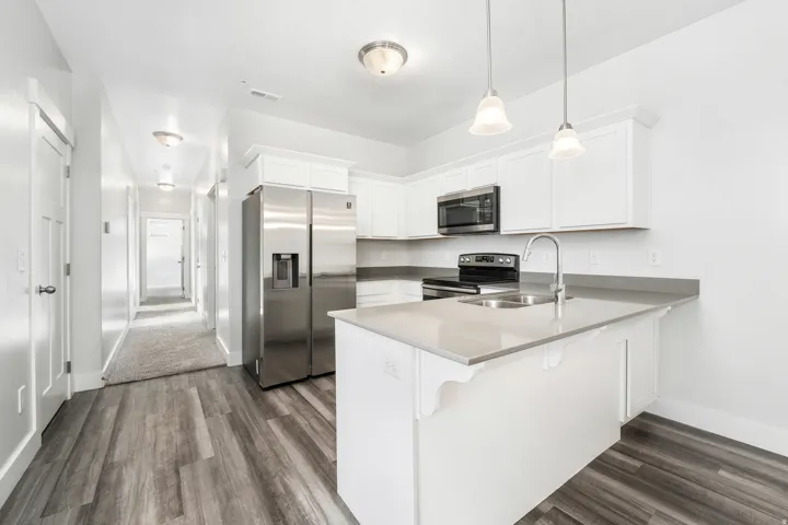 Modern kitchen featuring white cabinetry, light-toned countertops, stainless steel appliances, and a kitchen island with sink and pendant lighting