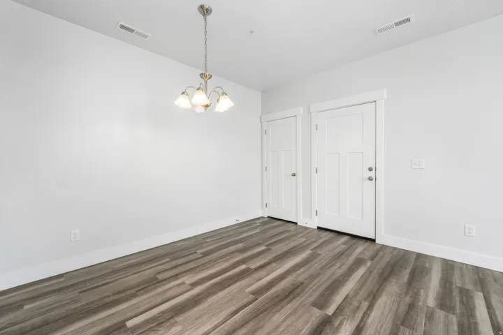 Interior space featuring wood-finish flooring, a contemporary chandelier, two panel doors with hardware, white baseboards, and white walls
