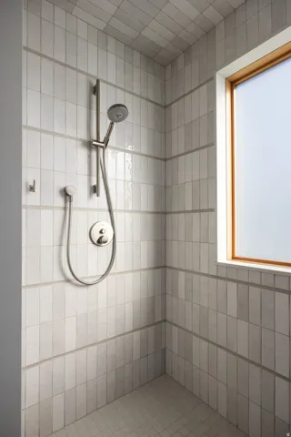 Shower stall featuring vertical rectangular wall tiling with horizontal grout accents, a rain shower head, a handheld shower head, and a wood-framed window