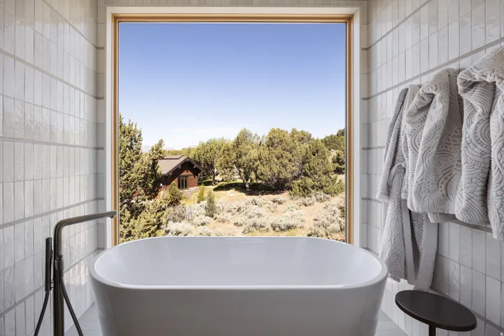 Freestanding soaking tub with a floor-mounted faucet, surrounded by vertically oriented tile walls
