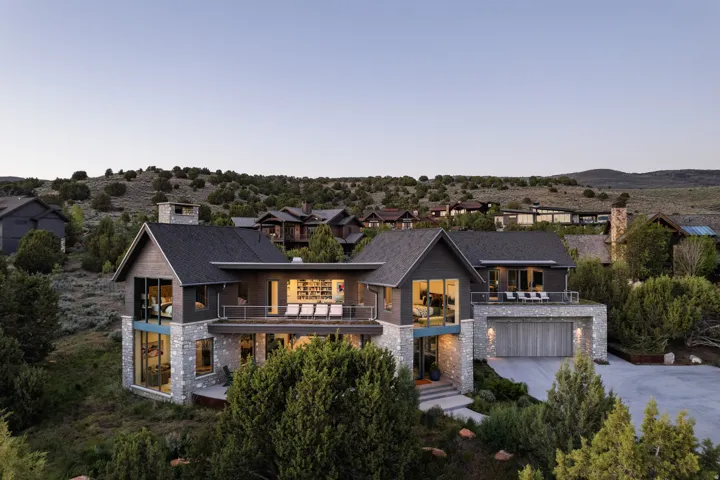 Modern architectural property featuring a stone and dark siding facade, multiple balconies, an integrated garage, and extensive windows