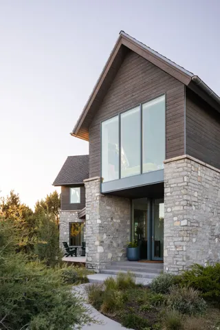 Modern architectural design featuring stone and wood-panel siding, a prominent gabled roofline, and large format windows
