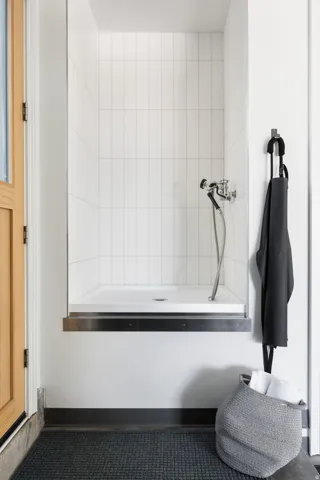 Elevated shower stall featuring white vertical subway tile, a chrome shower fixture with a handheld sprayer, and a white shower pan