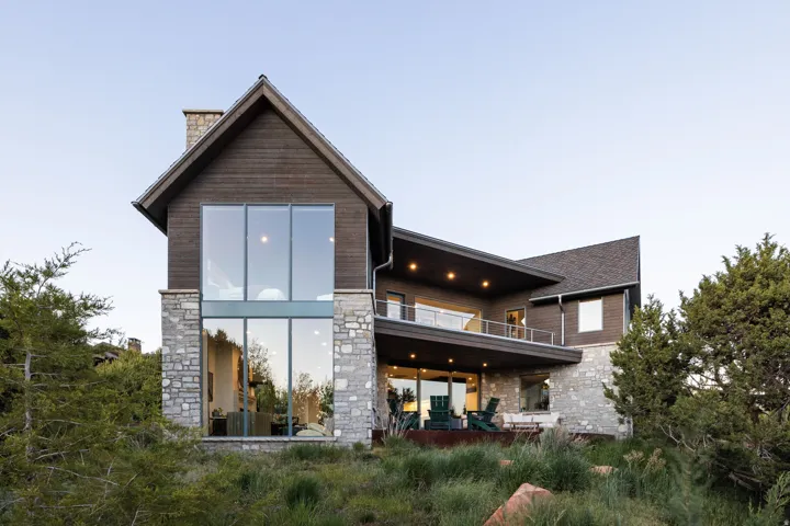Contemporary architectural design featuring a prominent two-story window wall, natural stone accents, horizontal wood siding, and a spacious outdoor balcony with glass railings