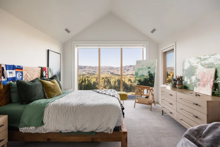 Bedroom with vaulted ceilings, a large picture window, and a secondary window offering expansive landscape scenery