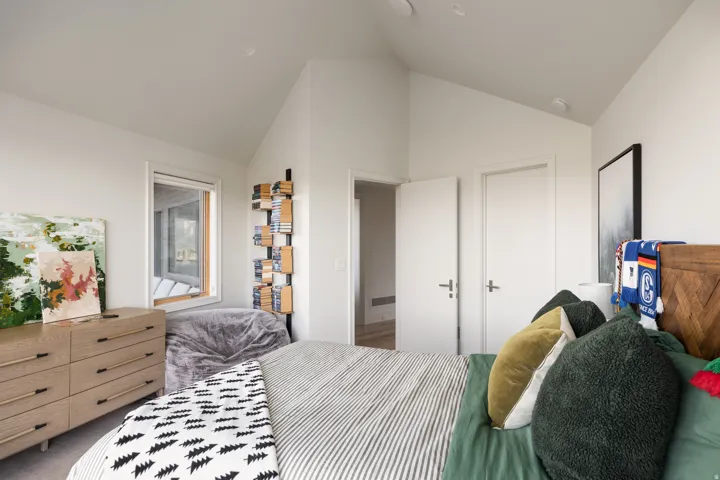 Vaulted ceiling room featuring light wood-finish flooring, a contemporary window with wood trim, and sleek white interior doors