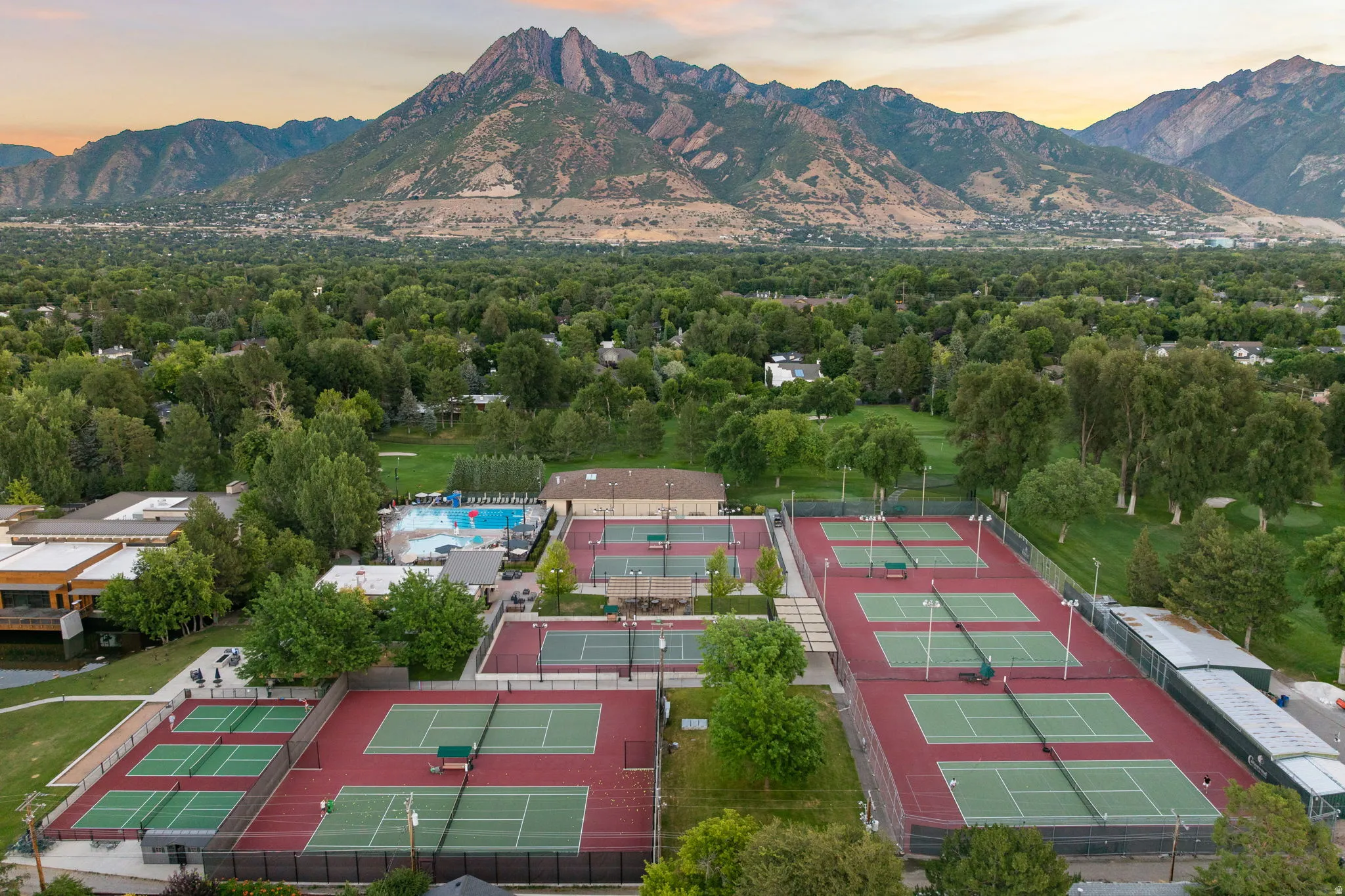 Extensive sports complex featuring multiple tennis courts, an outdoor swimming pool, and surrounding green spaces