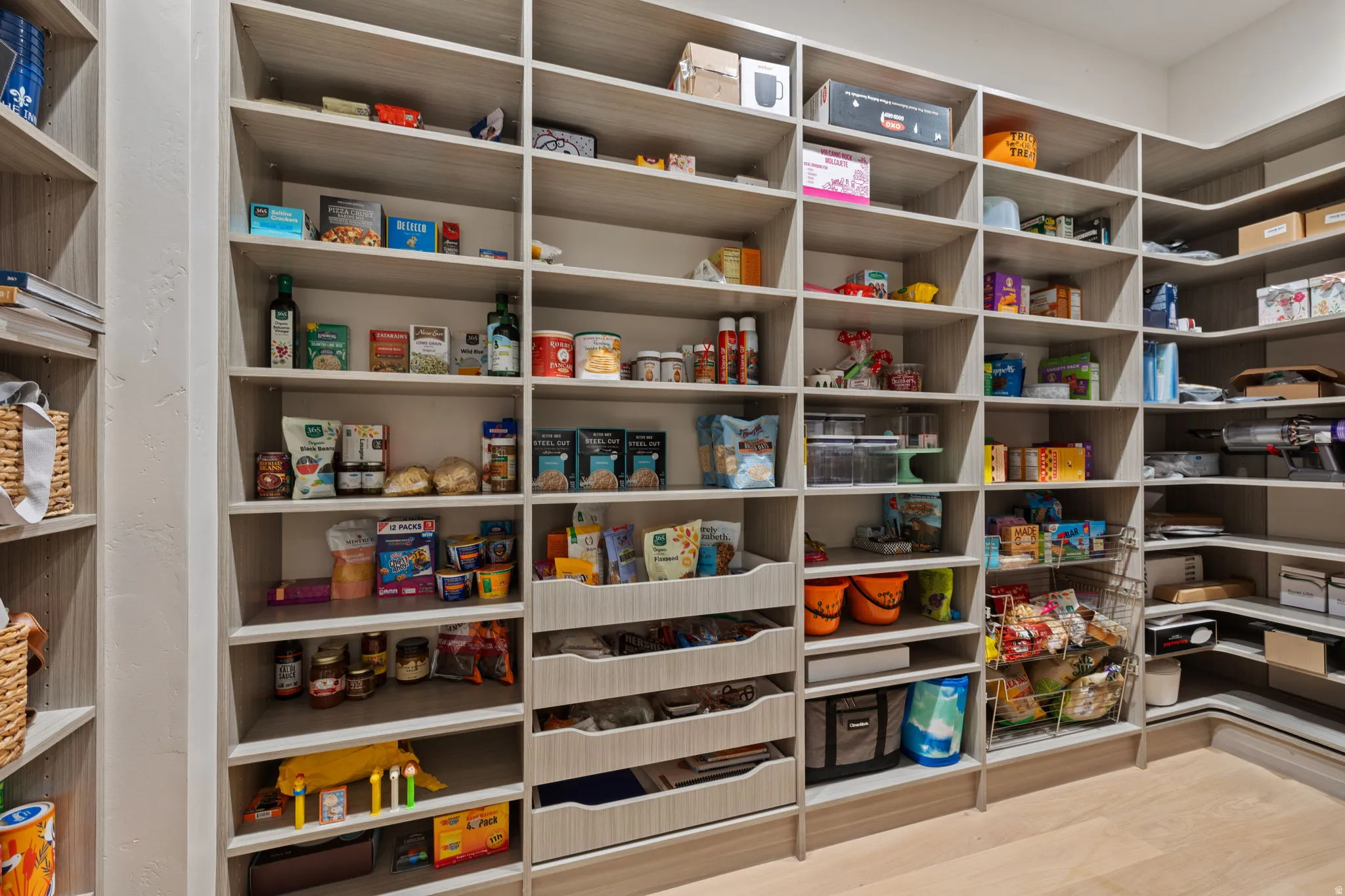 Expansive walk-in pantry featuring extensive built-in shelving, integrated drawers, durable wood-finish flooring, and recessed ceiling lighting