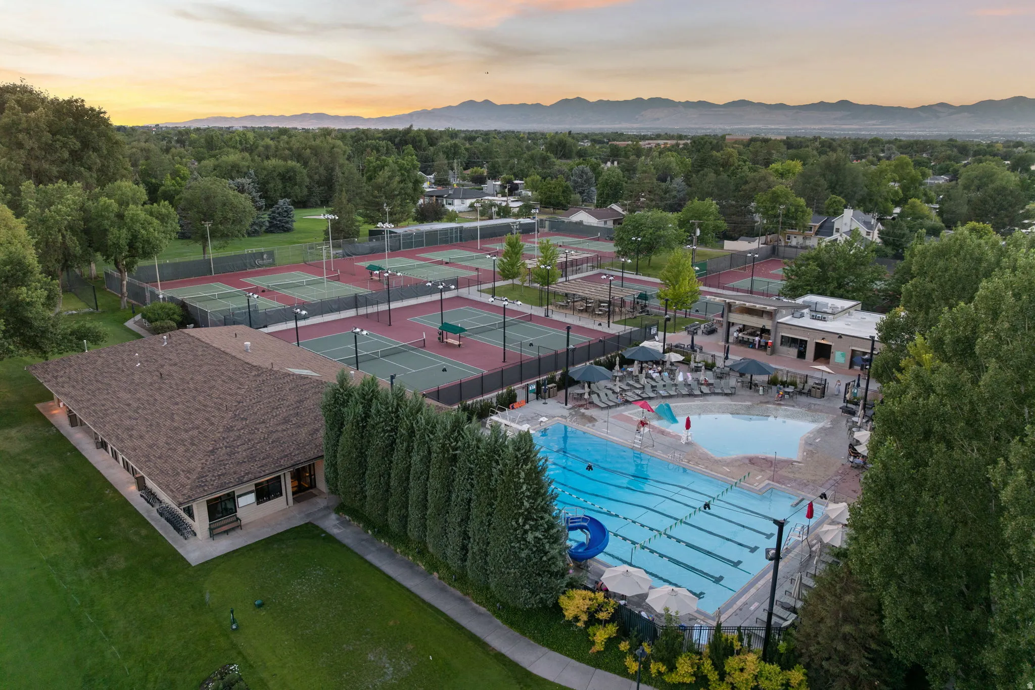 Expansive recreational grounds featuring multiple tennis courts, a large outdoor swimming pool with lane lines, a separate shallow pool area, and surrounding mature trees