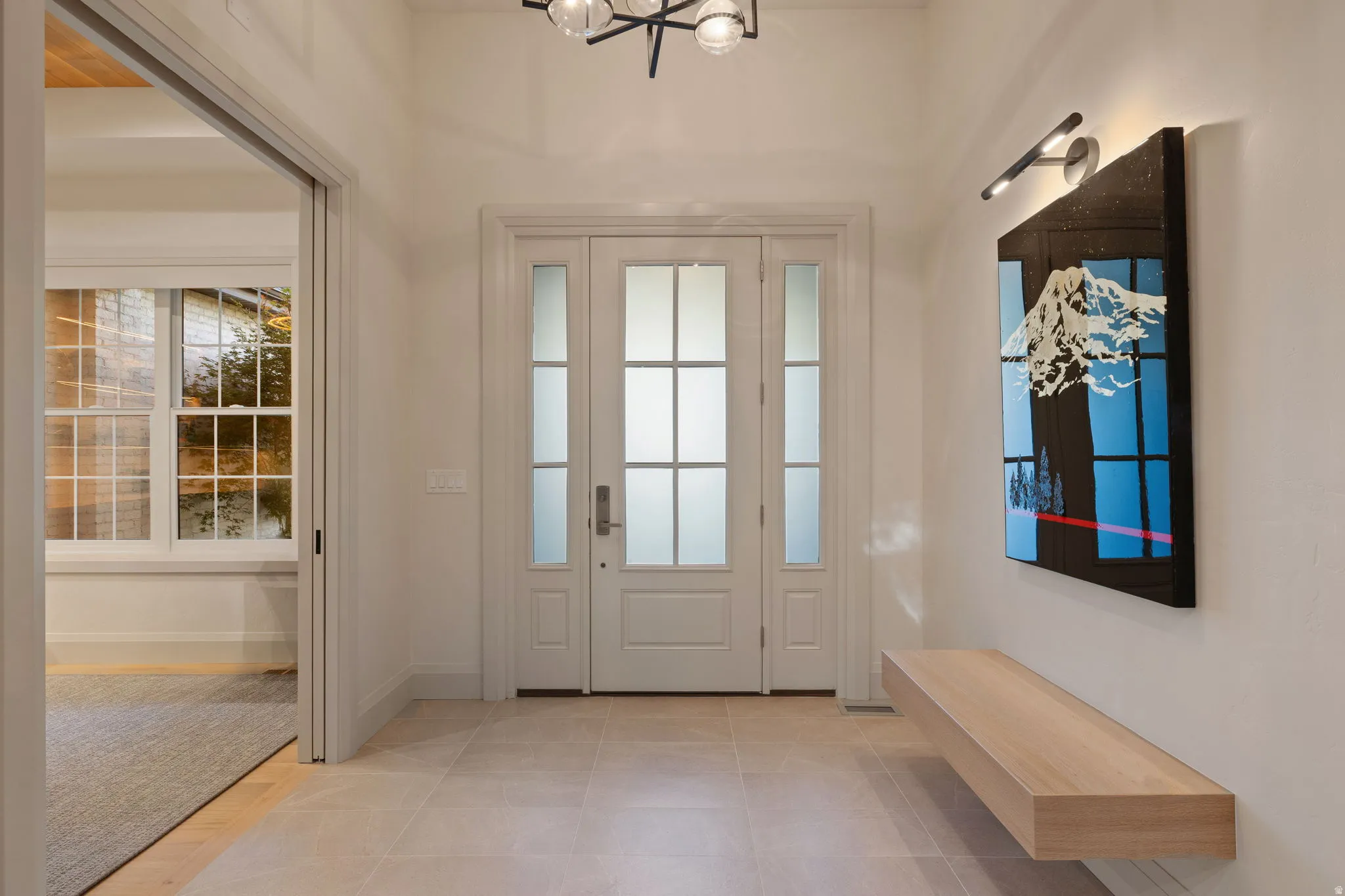 Foyer featuring light-toned tile flooring, a contemporary chandelier, and a floating wood-finish bench
