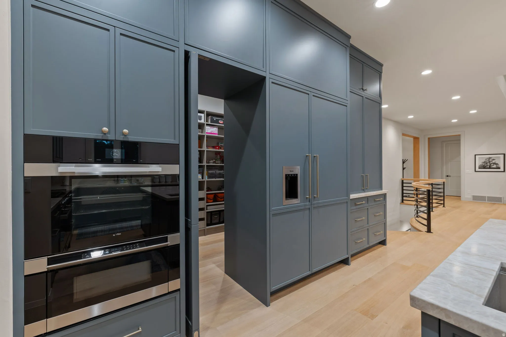 Modern kitchen featuring blue-gray cabinetry, built-in double ovens, and an integrated refrigerator