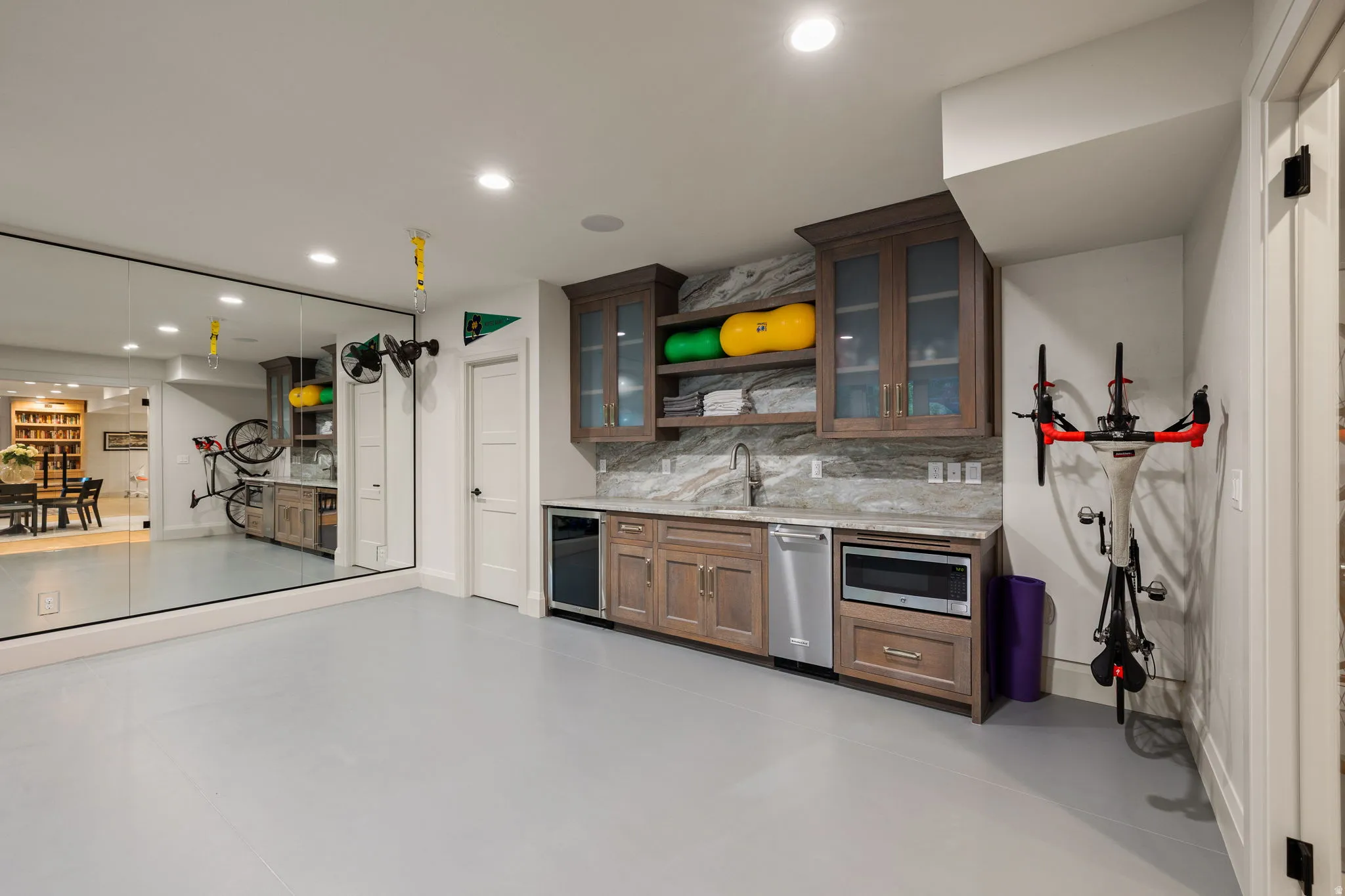 Spacious recreational room featuring a full mirrored wall, light gray flooring, and recessed lighting