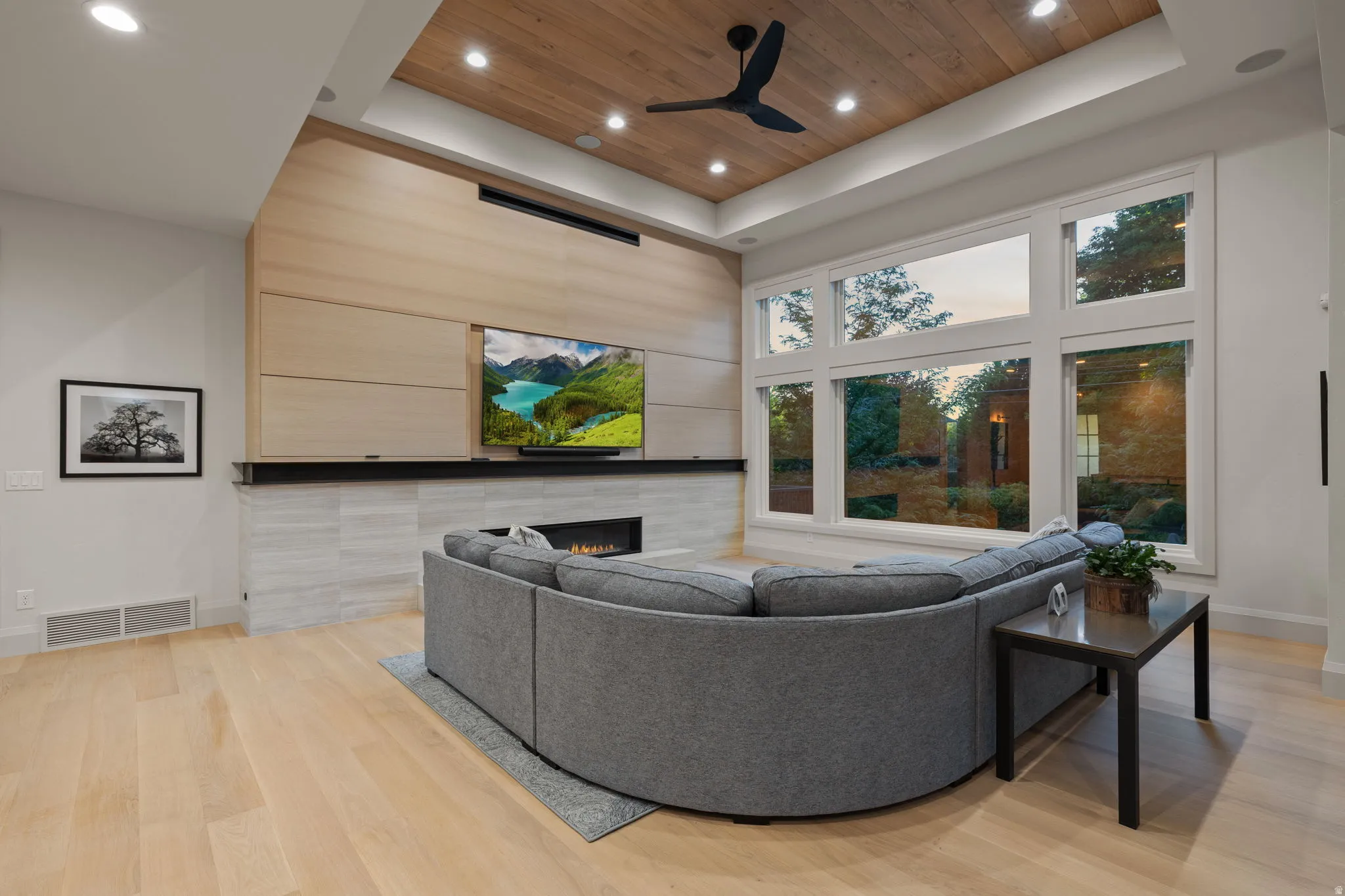Spacious living area featuring a wood-finish ceiling with recessed lighting, large picture windows, a modern linear fireplace, and light wood-finish flooring