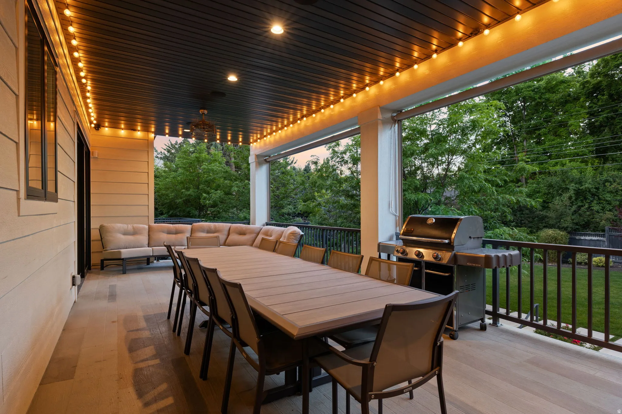 Spacious covered outdoor patio featuring light wood-finish flooring, a dark paneled ceiling with recessed lighting, and an overhead fan
