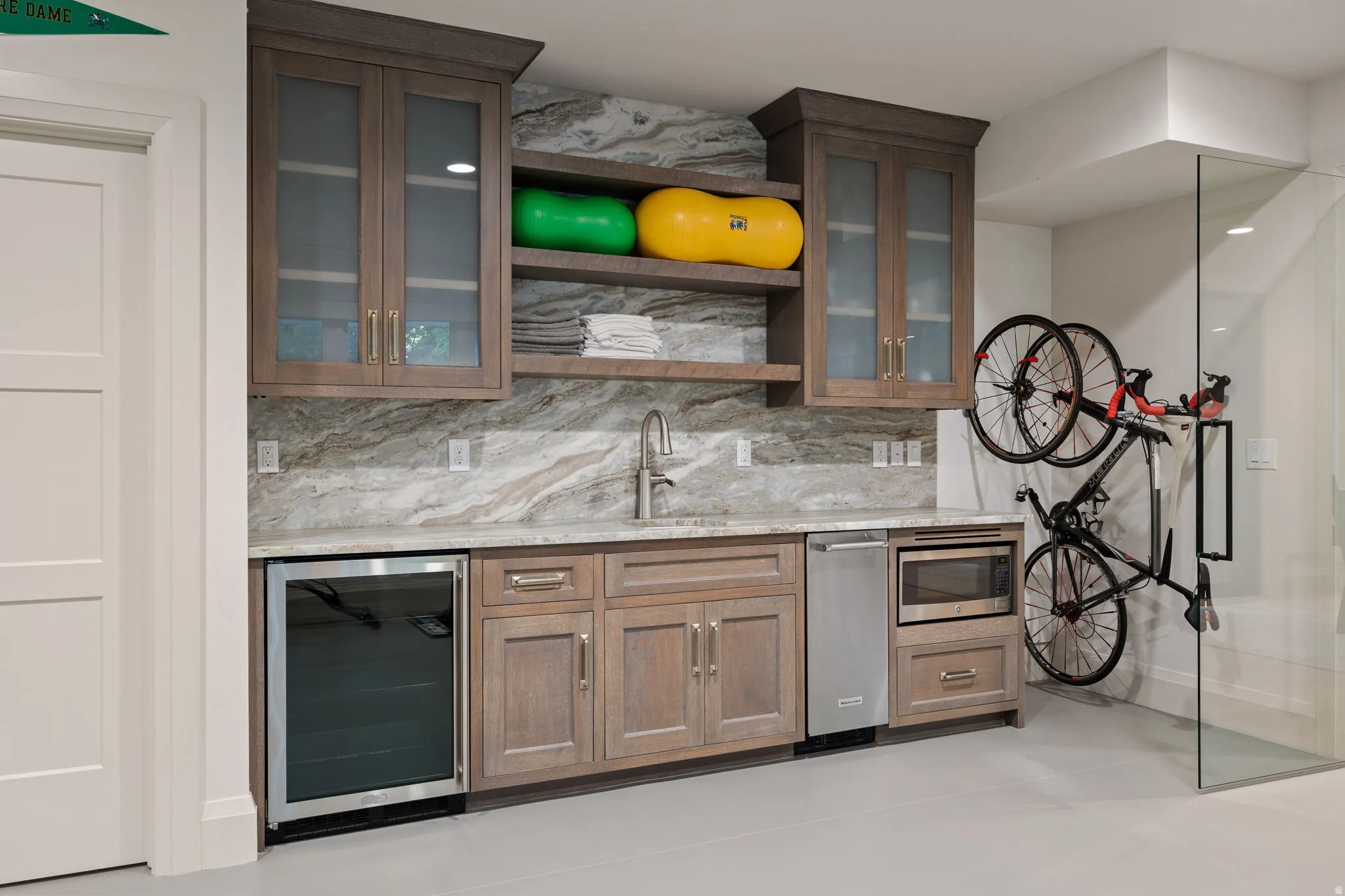 Custom built-in cabinetry with frosted glass doors, a stone backsplash, integrated sink, and under-counter beverage refrigerator