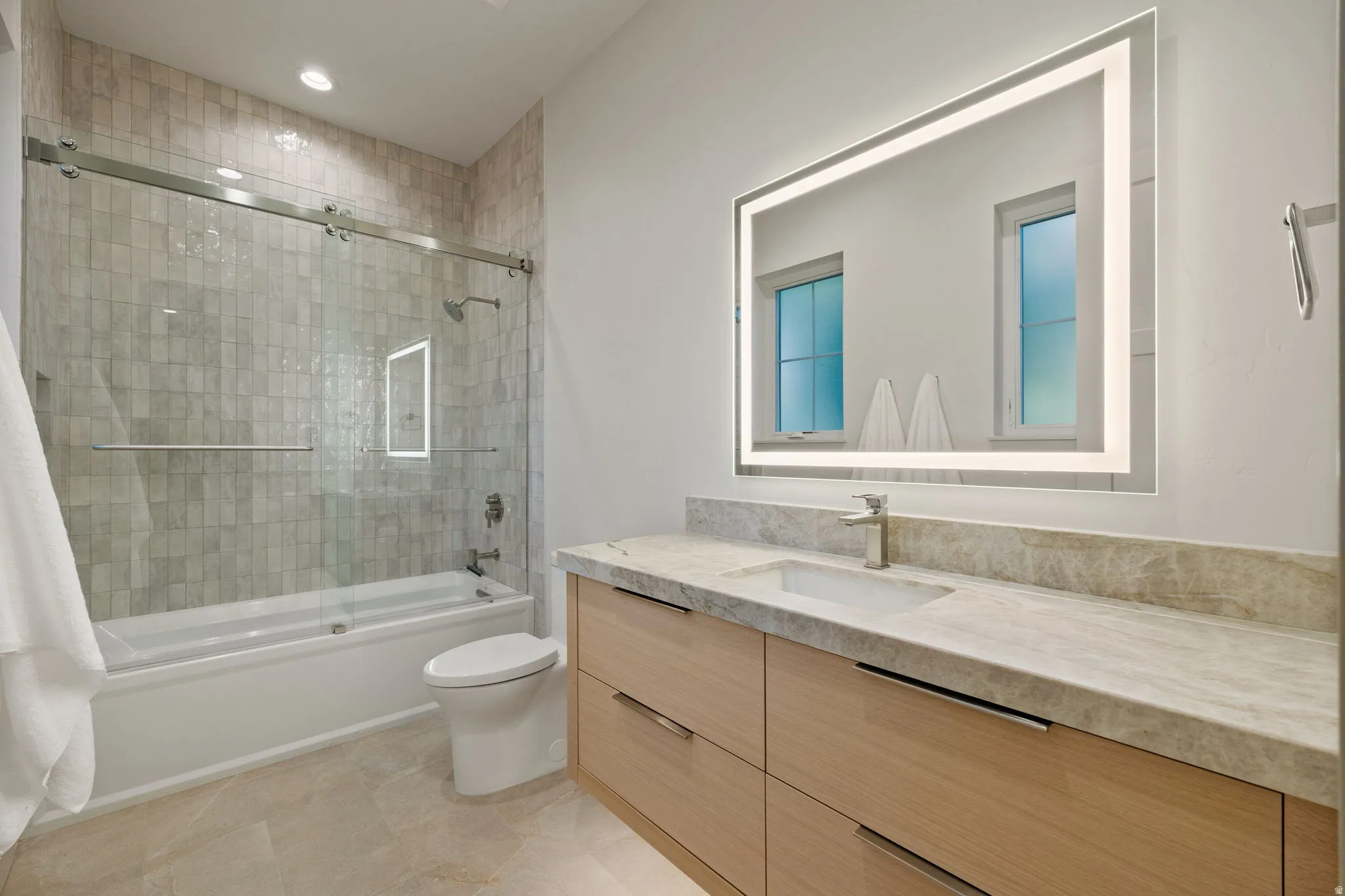 Contemporary bathroom featuring a light wood-finish vanity with an integrated rectangular sink and stone countertop