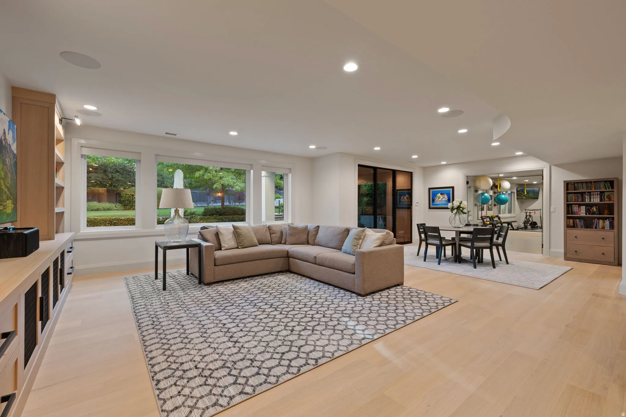 Spacious open-concept room featuring light wood-finish flooring, recessed lighting, and a wall of windows