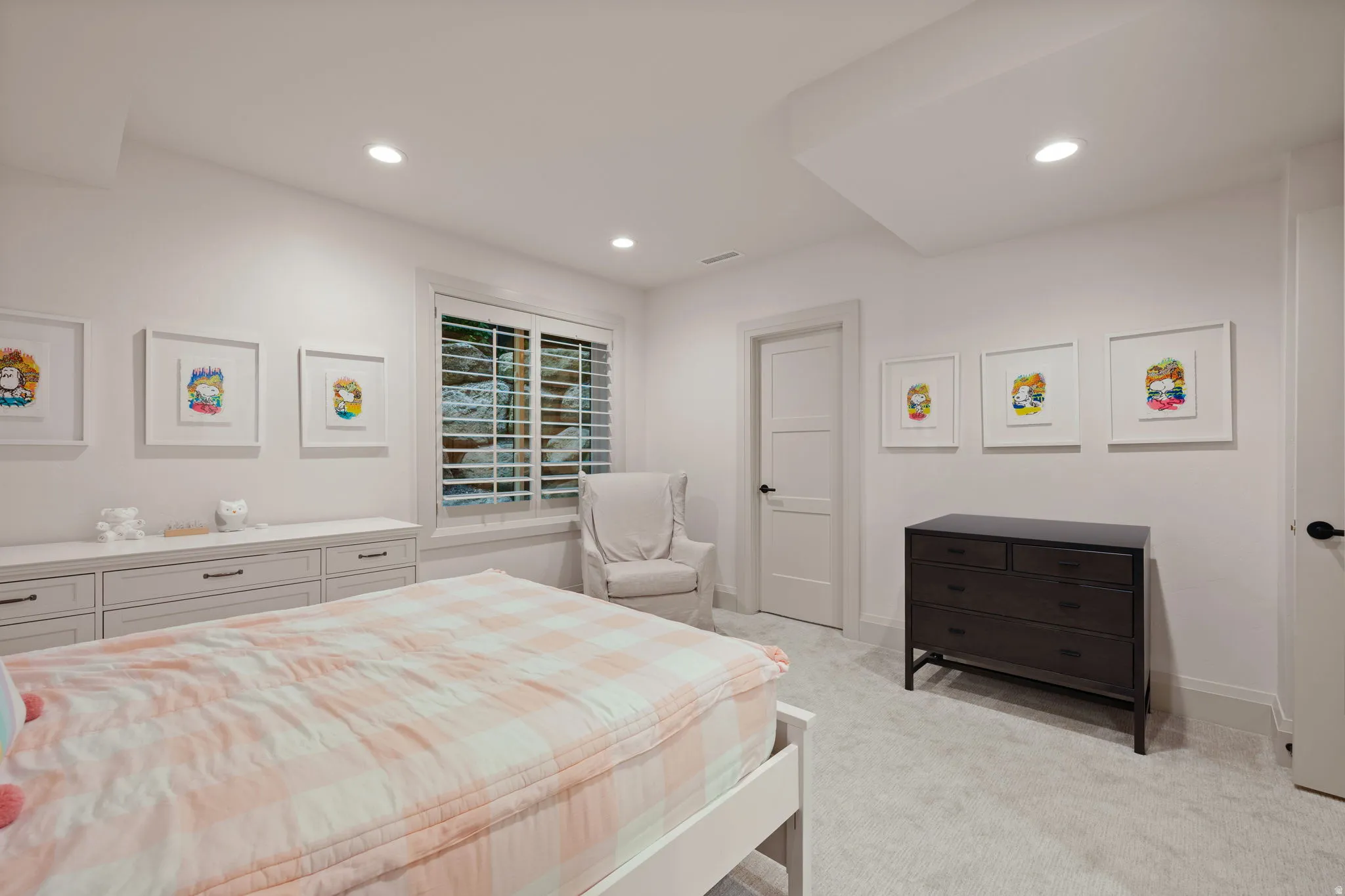 Bedroom featuring light gray carpeting, recessed ceiling lighting, a window with white louvered shutters, and a three-panel interior door with matte black hardware